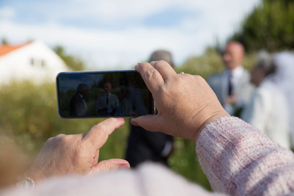The future of video in PR & comms (and what teams must prepare for) . A person holds a smartphone, capturing a wedding ceremony outdoors, with guests and greenery in the background.